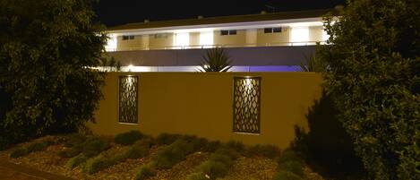 Un edificio con techo plano, ventanas rectangulares y un paseo pavimentado.