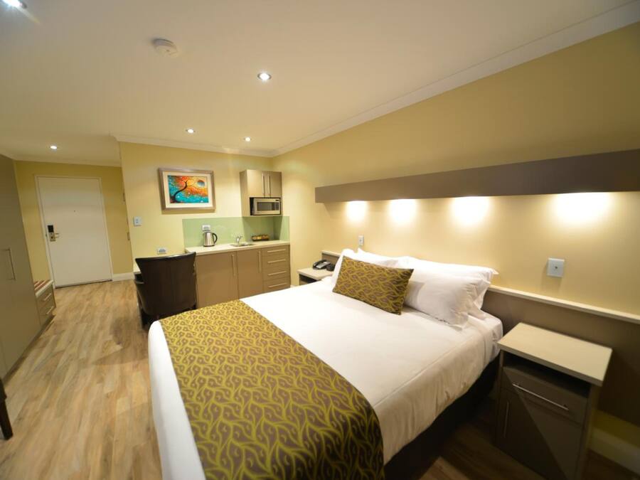 Una habitación de hotel con cama, mesita de noche y una pequeña cocina.