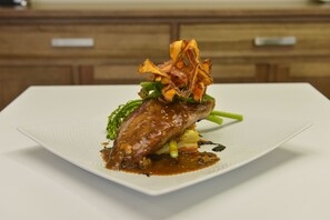 A square white plate with a dish of meat, vegetables, and sauce.