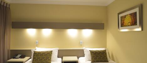 A hotel room with two single beds, a bedside table with a phone, and a wall-mounted light fixture.