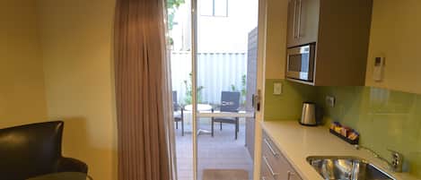 A compact kitchen with a sink, a microwave, and a dining area visible through a sliding door.