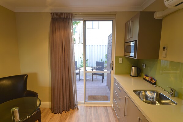 A compact kitchen with a sink, a microwave, and a dining area visible through a sliding door.