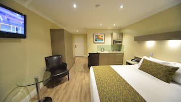 A hotel room with a bed, a desk, a chair, a television, and a kitchenette.