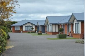 A row of modern, single-story buildings with flat roofs, arranged in a linear fashion along a paved driveway. - Tudor Lodge Motel (Hawera)