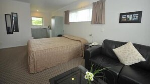 Quarto de hotel com cama, sofá de couro preto, pequena mesa com um vaso e janela com cortinas.