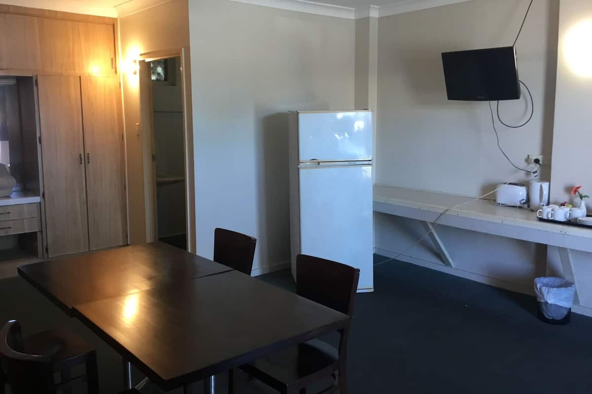 Una cocina compacta con refrigerador, una mesa de comedor, sillas, una pequeña encimera con tostadora y un televisor montado en la pared.