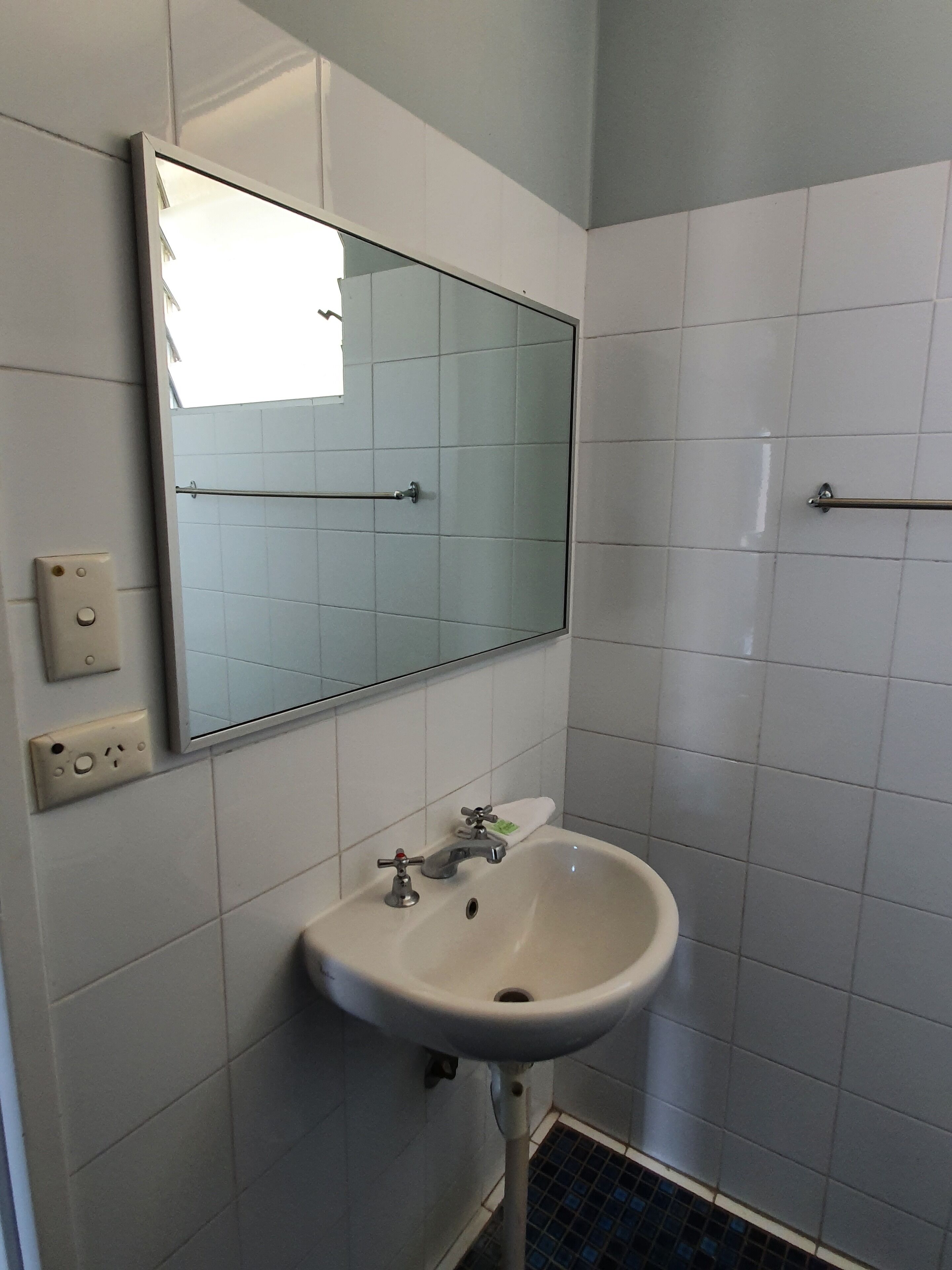 Un baño con lavamanos blanco, un espejo y piso de baldosas.