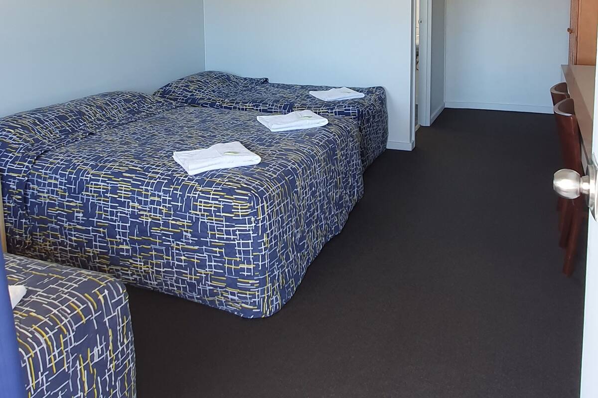 Una habitación con dos camas, ventilador de techo, aire acondicionado y una puerta.