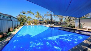 Piscina retangular com água azul cristalina, rodeada por espreguiçadeiras e plantas em vasos.