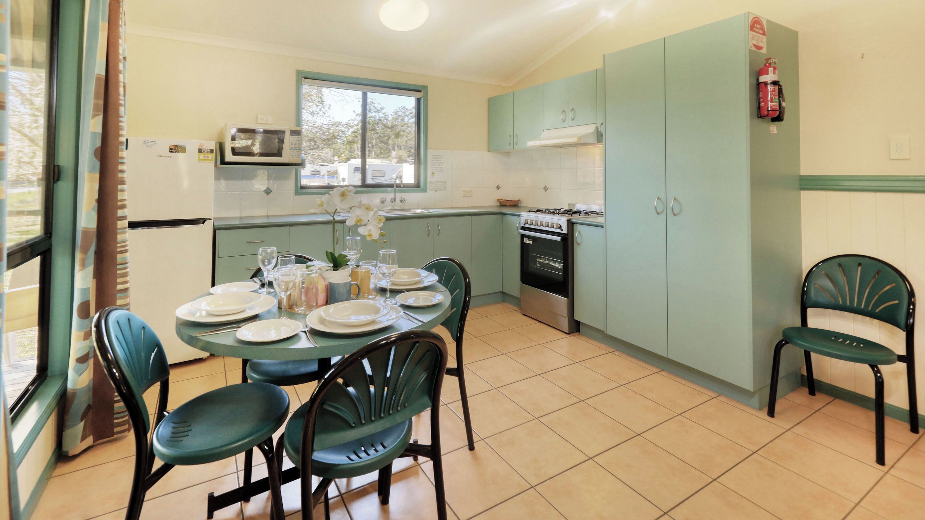 A compact kitchen with a dining table set for four, a microwave, a stove, and a fire extinguisher.