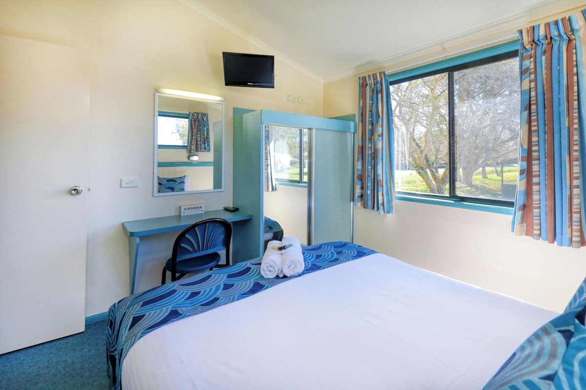 Ein Hotelzimmer mit Bett, Schreibtisch, Stuhl, Spiegel, Fernseher und einem Fenster mit Vorhängen.