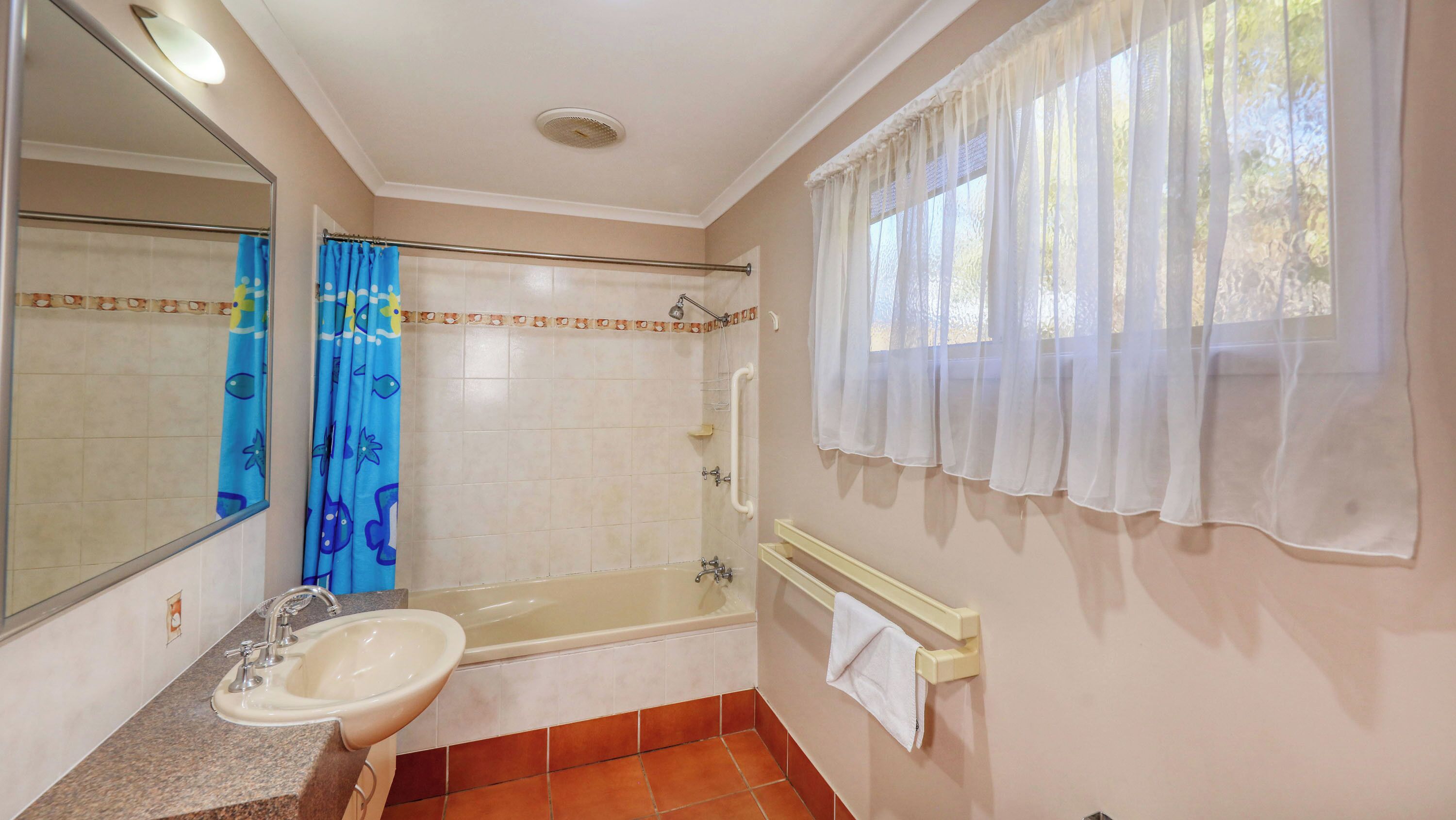 A bathroom with a sink, mirror, bathtub, and window with curtains.