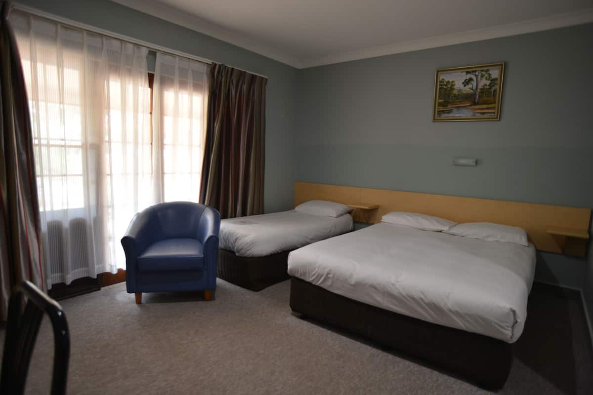 A hotel room with two single beds, a blue armchair, and a painting on the wall.
