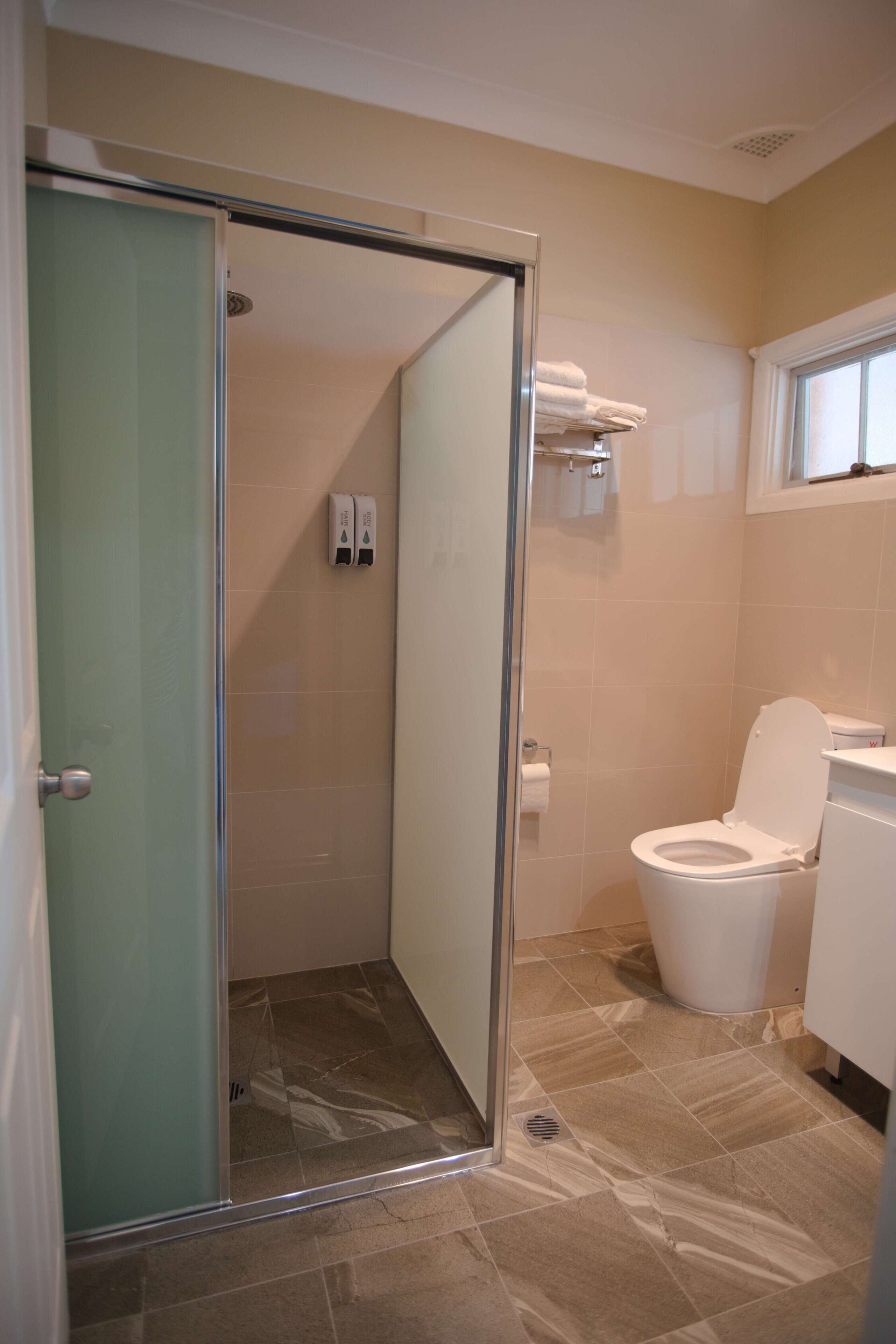 Un baño con mampara de vidrio, inodoro y lavamanos.