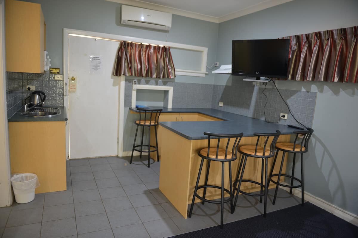 A compact kitchen with a built-in island, bar stools, a microwave, and a flat-screen TV mounted above the island.