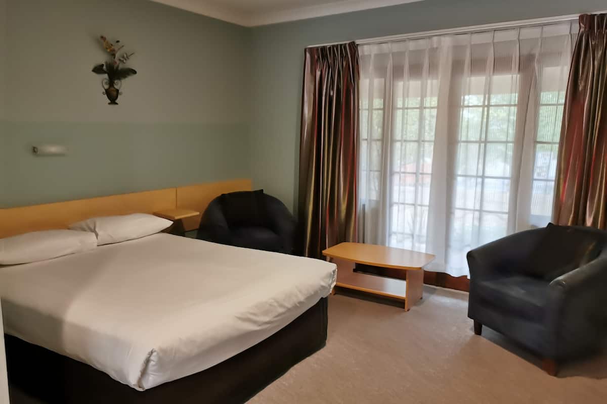 A hotel room with a bed, a desk, two chairs, and a window with curtains.