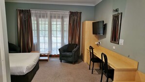 Una habitación pequeña con cama, escritorio, silla y televisión.