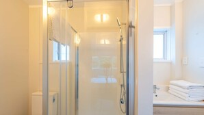 A modern bathroom with a glass-enclosed shower, a toilet, and a sink with stacked towels. - Ranfurly Evergreen Motel (Auckland)