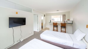 A hotel room with a bed, a desk with a chair, a television mounted on the wall, and a window with curtains. - Ranfurly Evergreen Motel (Auckland)