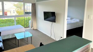 Une chambre d’hôtel avec un lit, un bureau, une chaise, une télévision et une fenêtre avec des rideaux.