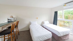 A room with two single beds, a desk with a chair, a window with curtains, and an air conditioning unit. - Ranfurly Evergreen Motel (Auckland)