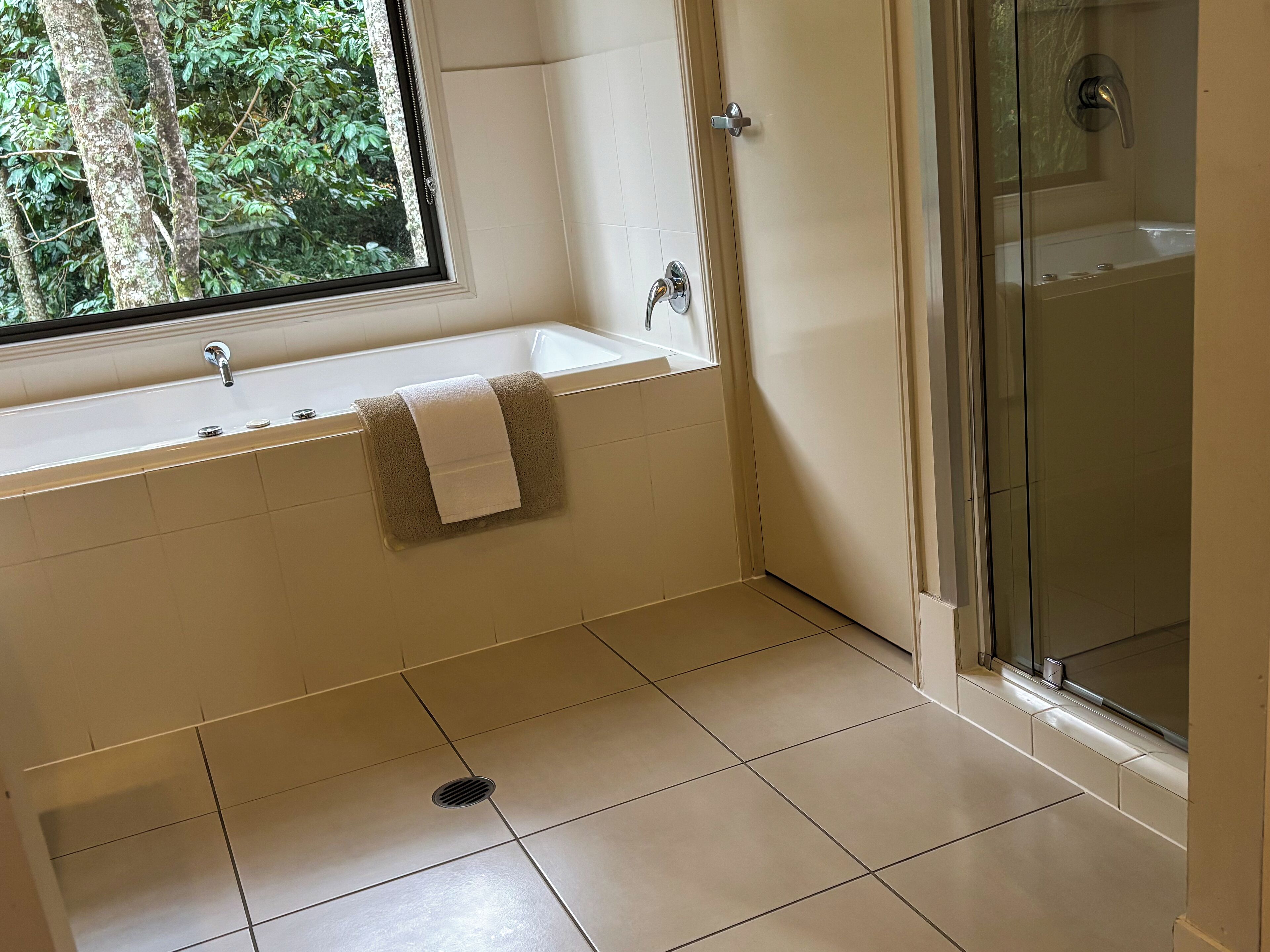 A bathroom with a bathtub, a shower, and a window with a view of trees.