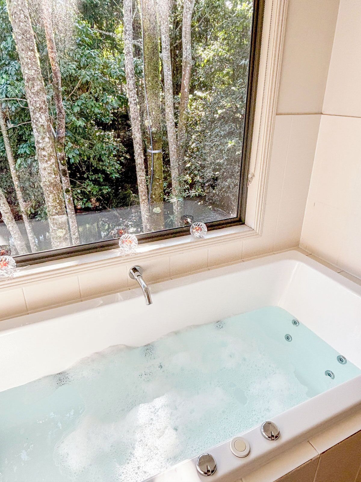 Une baignoire avec vue sur les arbres par la fenêtre.