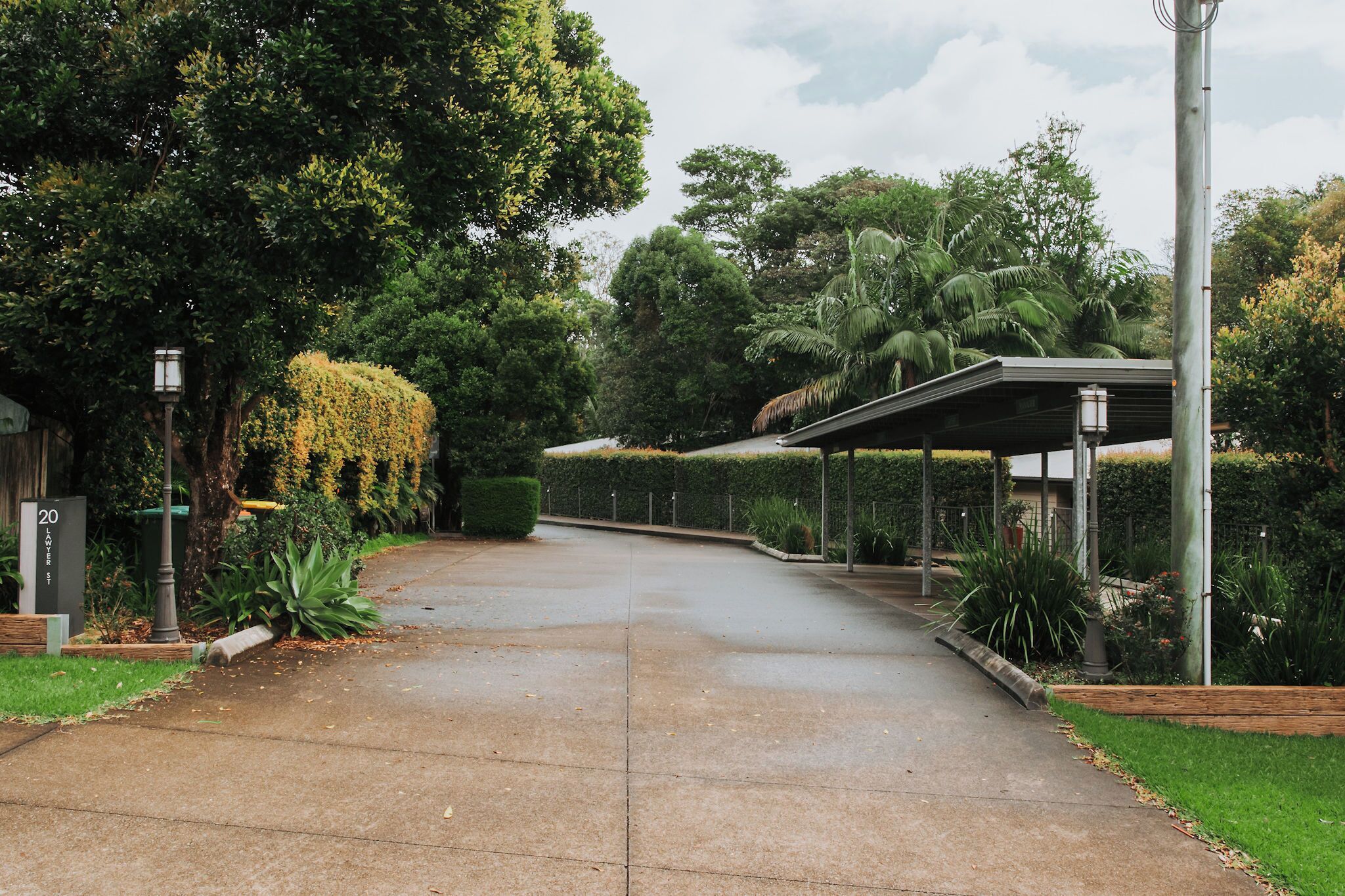 A paved pathway leading to a covered structure with a roof, surrounded by lush greenery and trees.