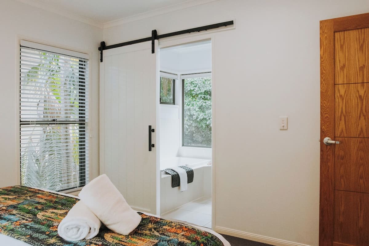A bedroom with a bed, a window with blinds, a sliding door to a balcony, and a wooden door.
