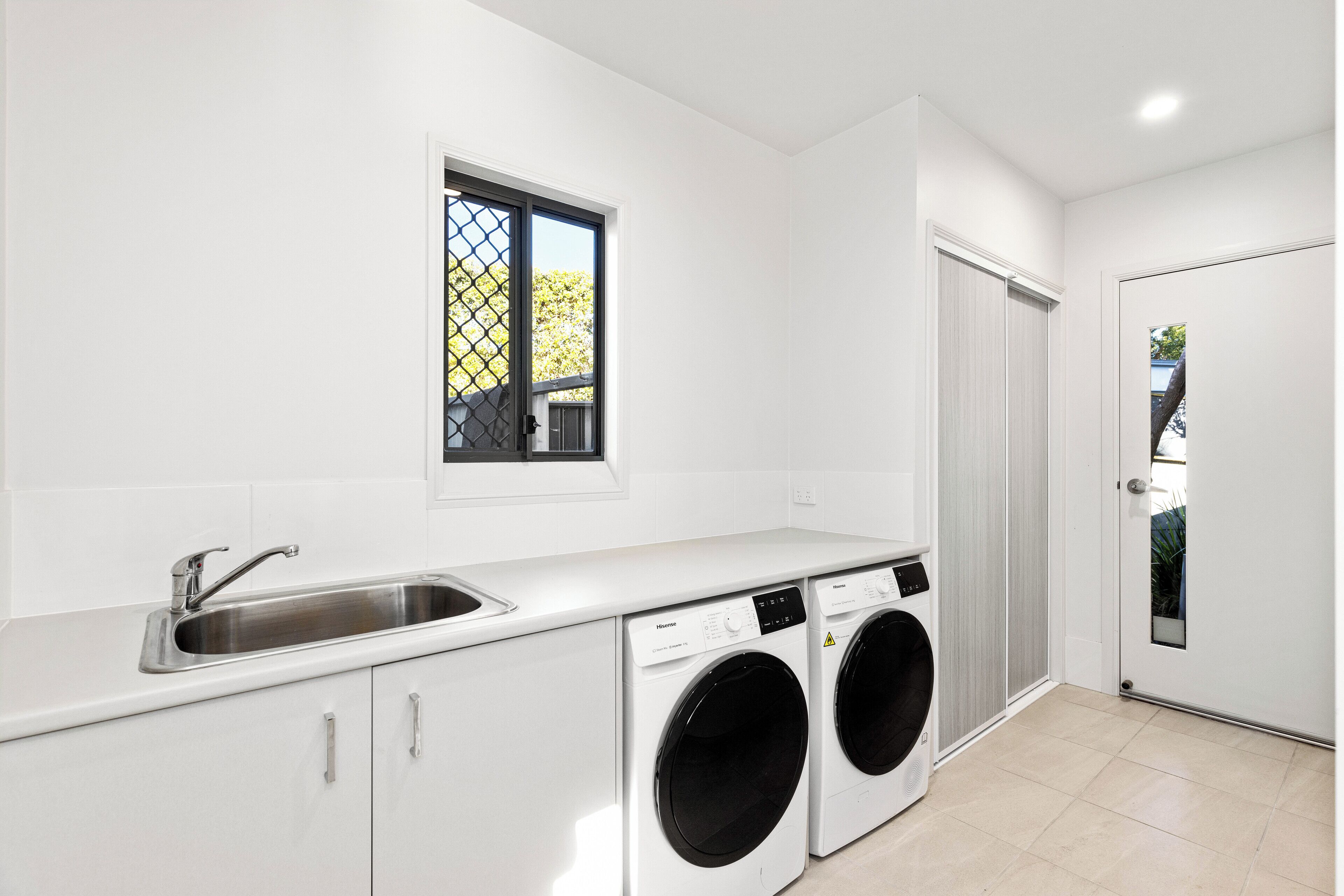 Una cocina moderna con lavadora integrada, un lavabo y una ventana con vistas a zonas verdes.