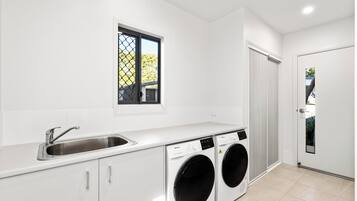 Una cocina moderna con lavadora integrada, un lavabo y una ventana con vistas a zonas verdes.