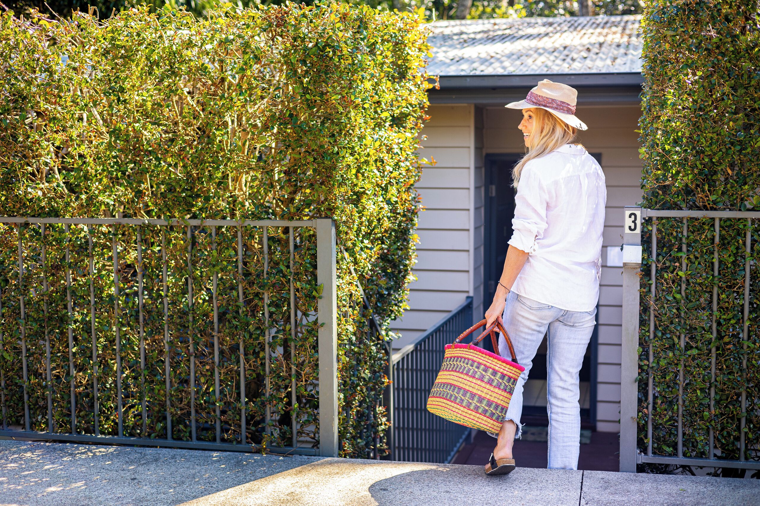 A person standing at a gated entrance with a house number 3, a metal gate, and a hedge.