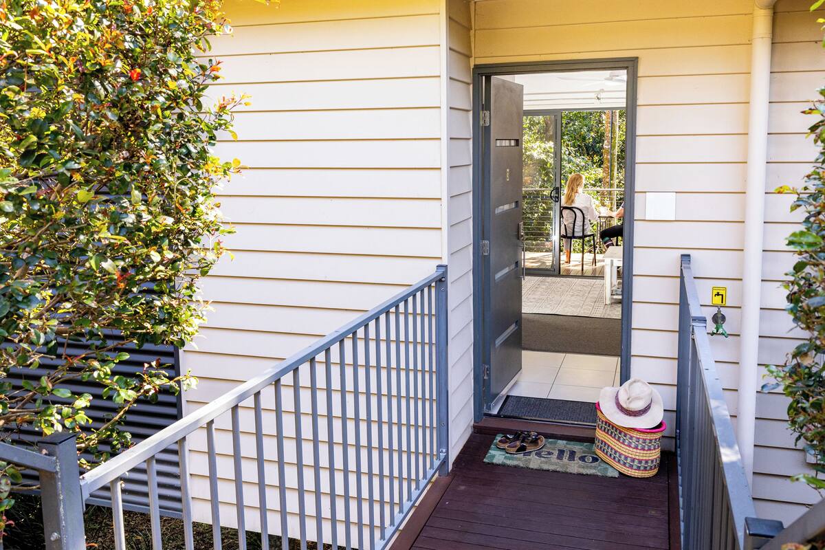 A wooden deck with a metal railing, a door leading to a covered patio, and a small basket with a hat on the ground.
