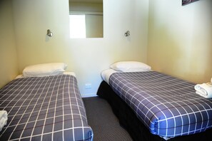 A room with two single beds, each with a pillow and a blanket.