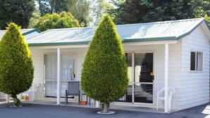 A small, single-story building with a green roof and white siding. There are two potted trees in front of the building, and a chair is visible inside. - Blenheim Bridges Holiday Park (Blenheim)