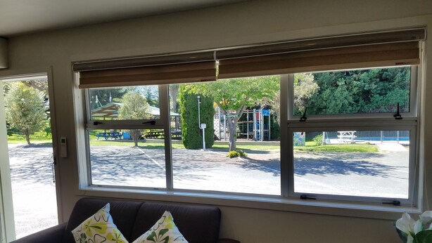 A room with a large window, a dark sofa with floral cushions, and a chair. - Blenheim Bridges Holiday Park (Blenheim)