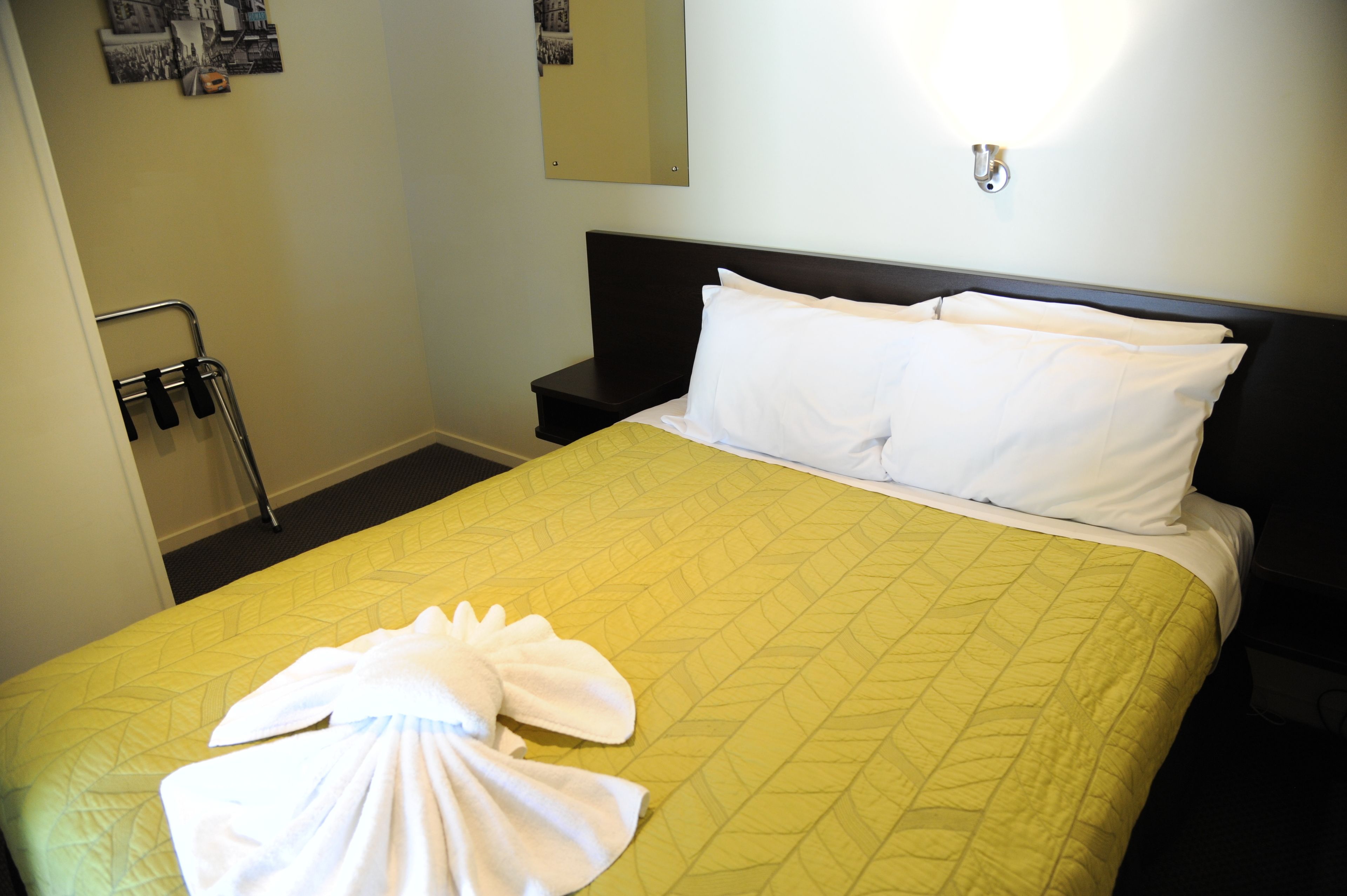 Habitación de hotel con cama, mesita de noche, luz empotrada en la pared y una toalla sobre la cama.