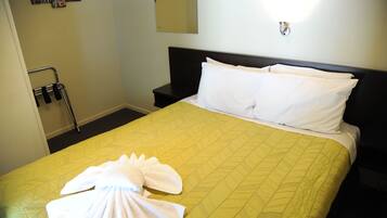 Habitación de hotel con cama, mesita de noche, luz empotrada en la pared y una toalla sobre la cama.