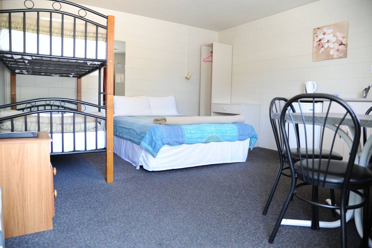 Ein Etagenbett mit blauer Decke, eine Holzkommode, ein Schreibtisch mit Stuhl und ein an der Wand befestigter Spiegel.