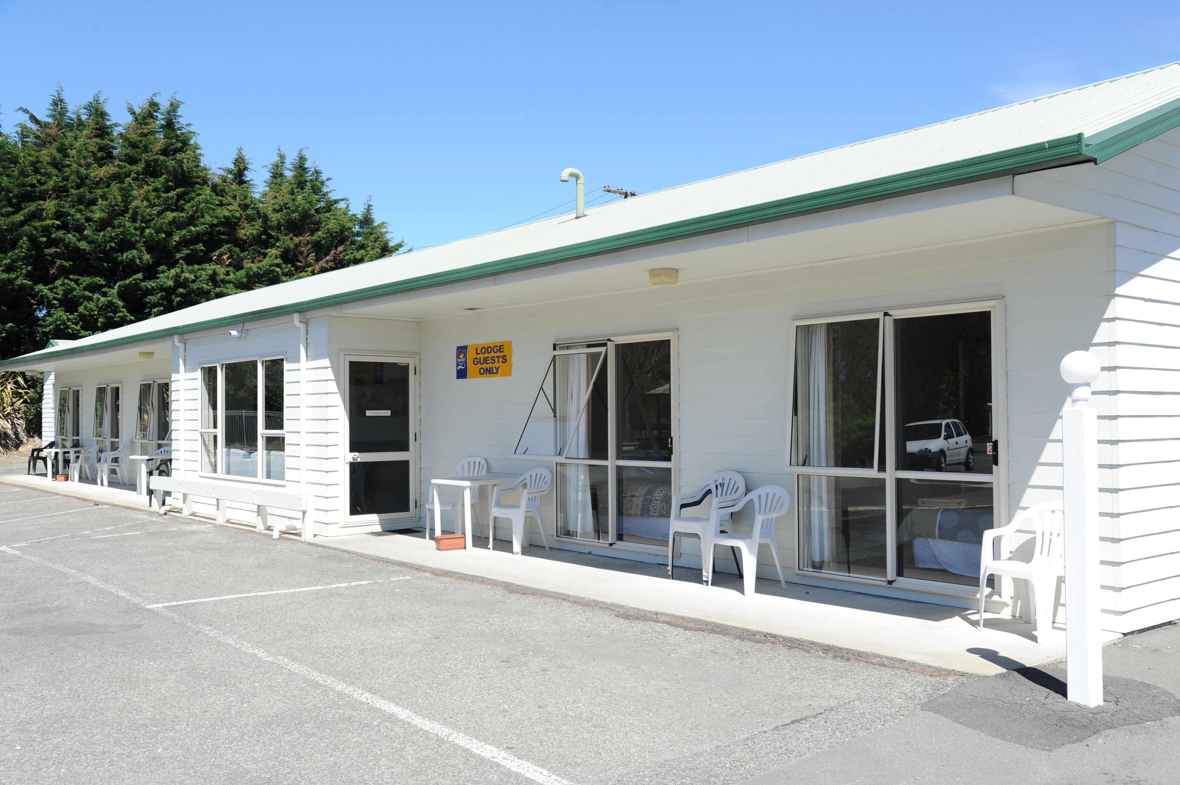 Ein Motel mit einer Reihe von eingeschossigen Zimmern, jedes mit Fenster und Tür. Es gibt Sitzbereiche im Freien mit weissen Kunststoffstühlen und -tischen.