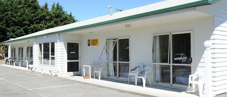 Ein Motel mit einer Reihe von eingeschossigen Zimmern, jedes mit Fenster und Tür. Es gibt Sitzbereiche im Freien mit weissen Kunststoffstühlen und -tischen.