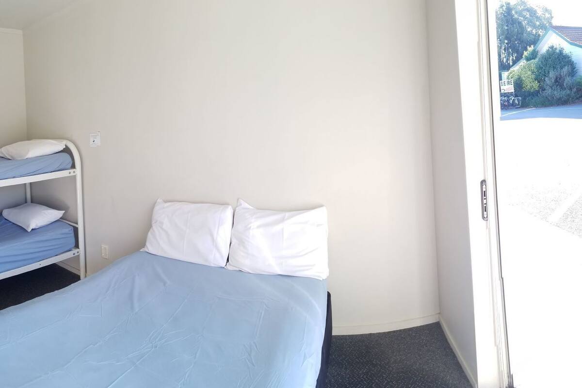 Ein kleines Hotelzimmer mit einem Stockbett, einem Fenster mit Blick nach draußen und einer Tür mit einem grünen Schild.