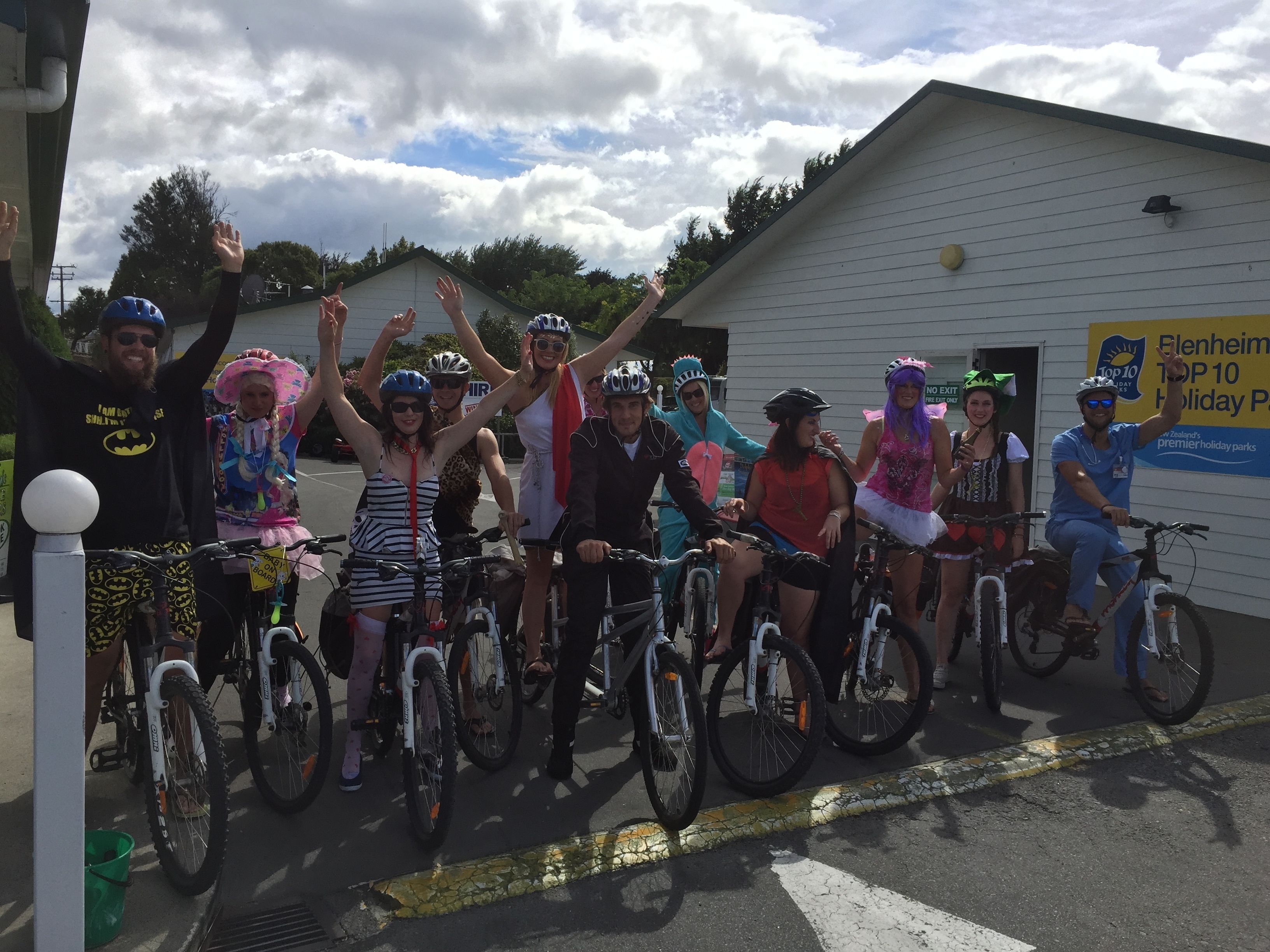Um grupo de pessoas de bicicleta em frente a um edifício com uma placa que diz 'Elenheim Top 10 Holiday Park'.