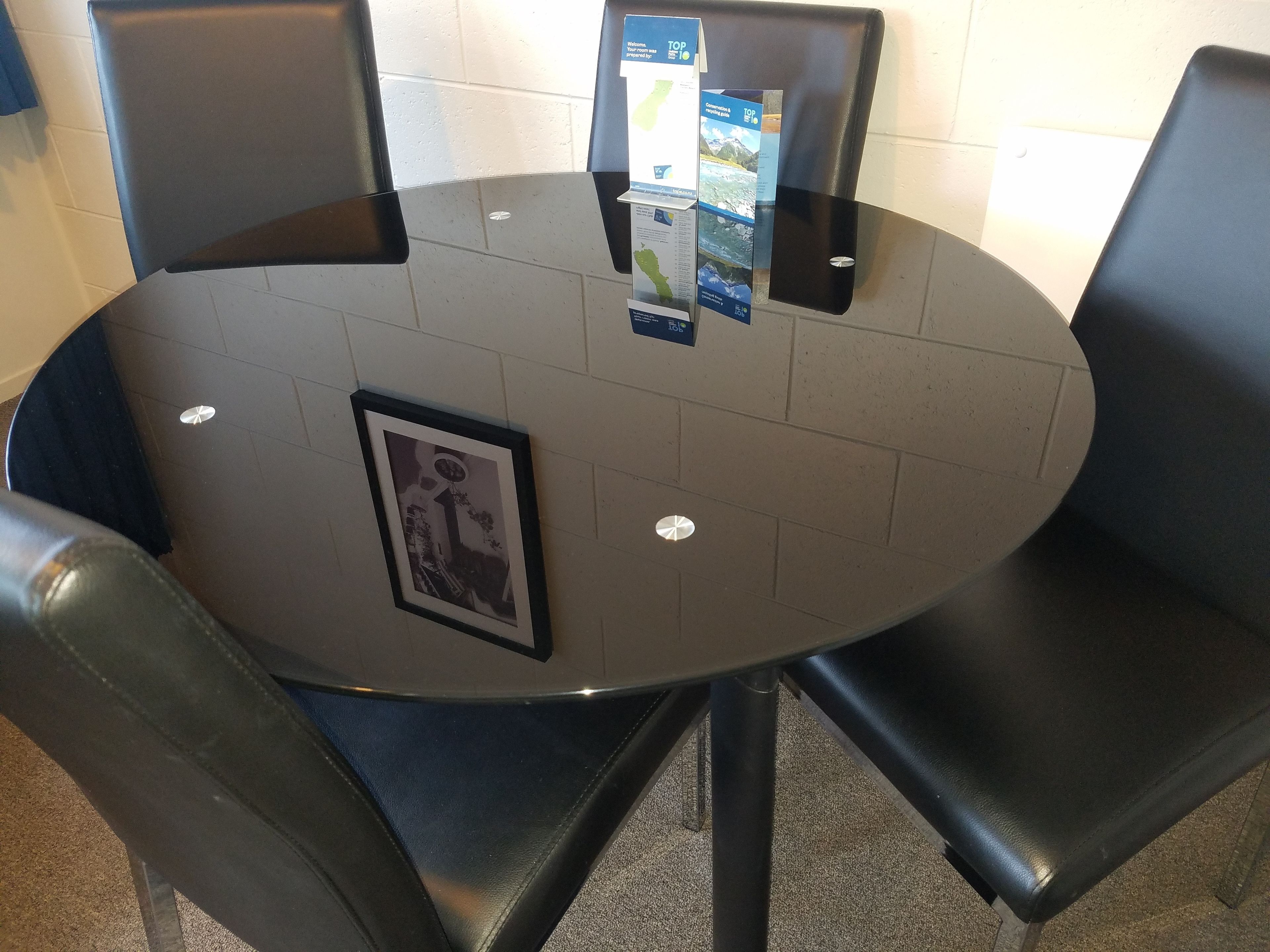 A round table with a black top and four black chairs. There is a framed picture on the table.