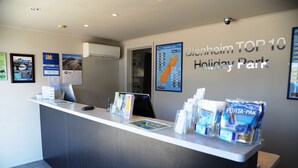 A reception desk at Blenheim TOP 10 Holiday Park with a computer, brochures, and a sign indicating the location. - Blenheim Bridges Holiday Park (Blenheim)