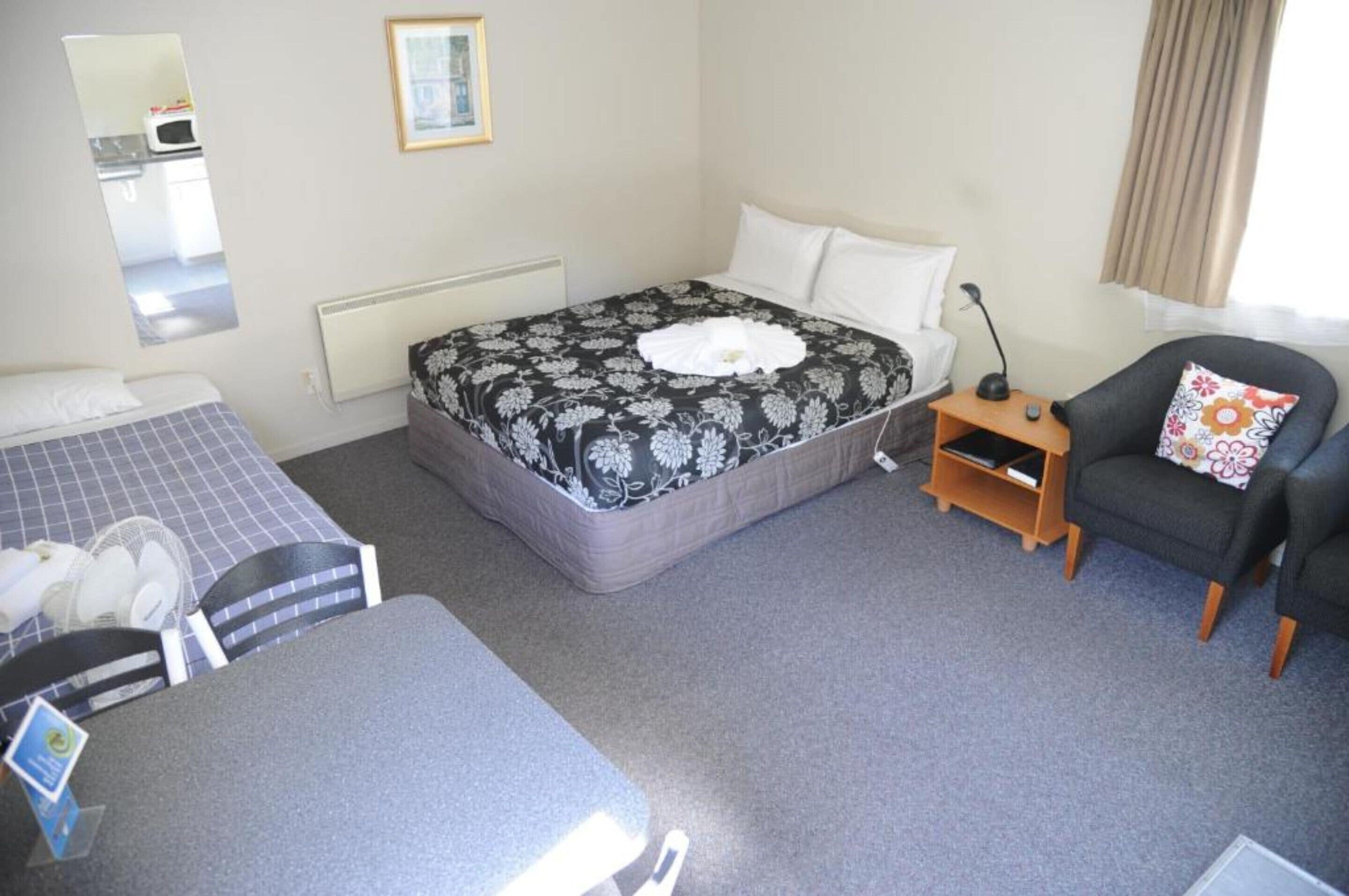 Een hotelkamer met een bed, een stoel, een klein tafeltje, een spiegel en uitzicht op de keuken.
