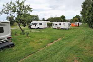 Ein Campingplatz mit Reisemobilen und Wohnwagen, auf einer grünen Wiese gelegen, umgeben von Bäumen und blauem Himmel.