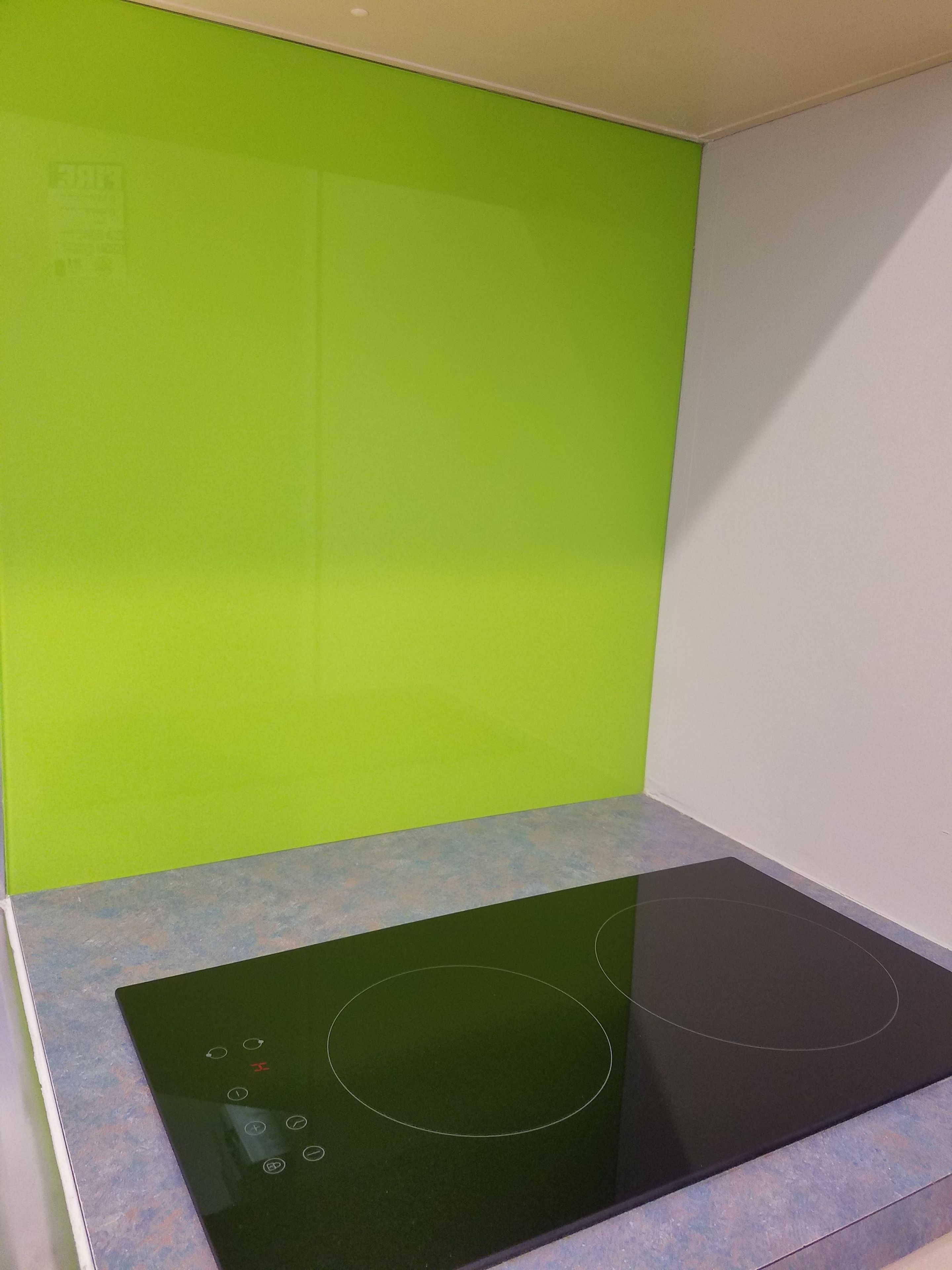 A kitchen with a black induction cooktop and a green backsplash.