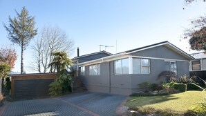A modern single-story house with a garage, a small front yard with a palm tree, and a clear sky. - B&B @ the Redwoods (Rotorua)