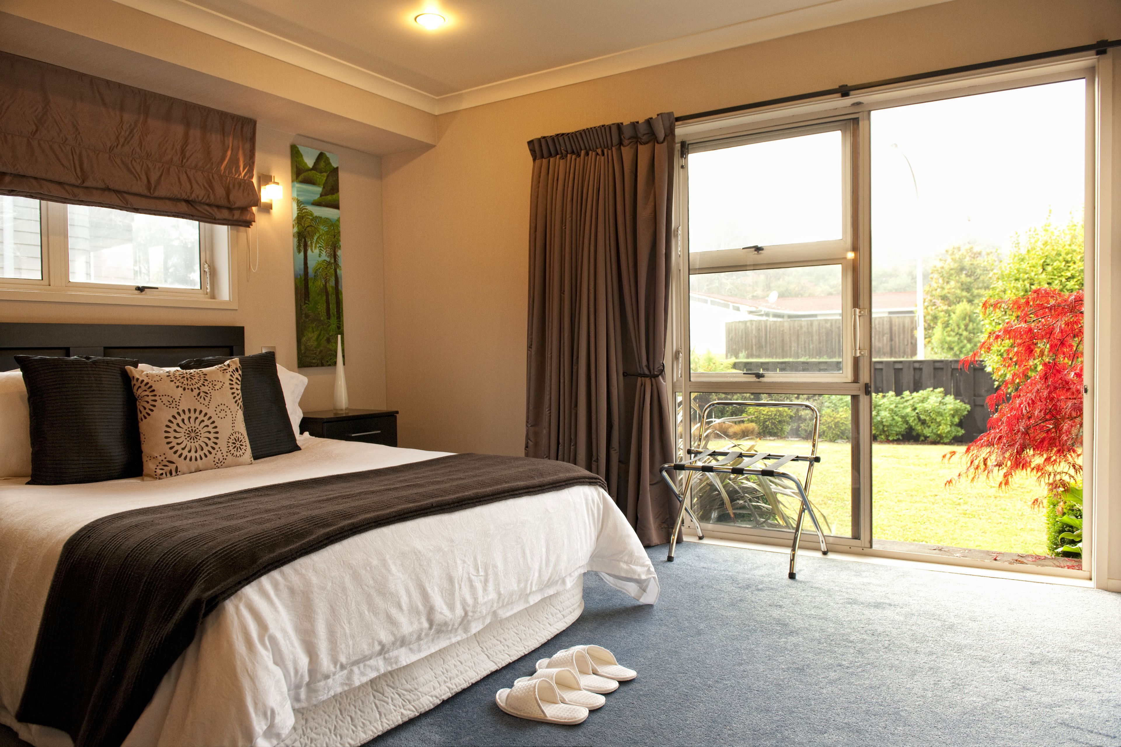 Un dormitorio con una cama grande, una ventana con cortinas y vistas a un jardín.